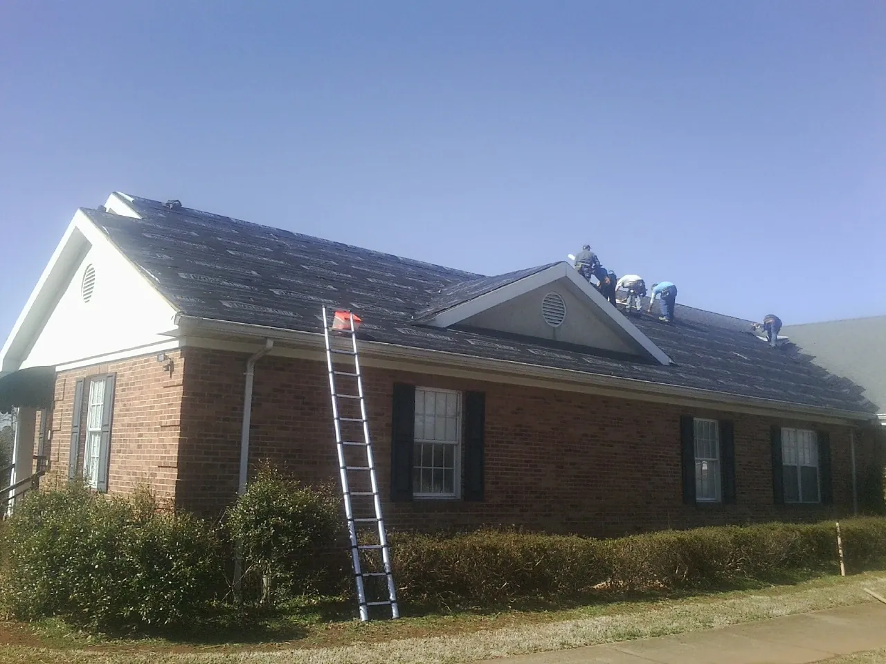 Crew tearing shingles off a brick ranch roof with a ladder set — Emergency Roof Repair work by our crew in Lakeville